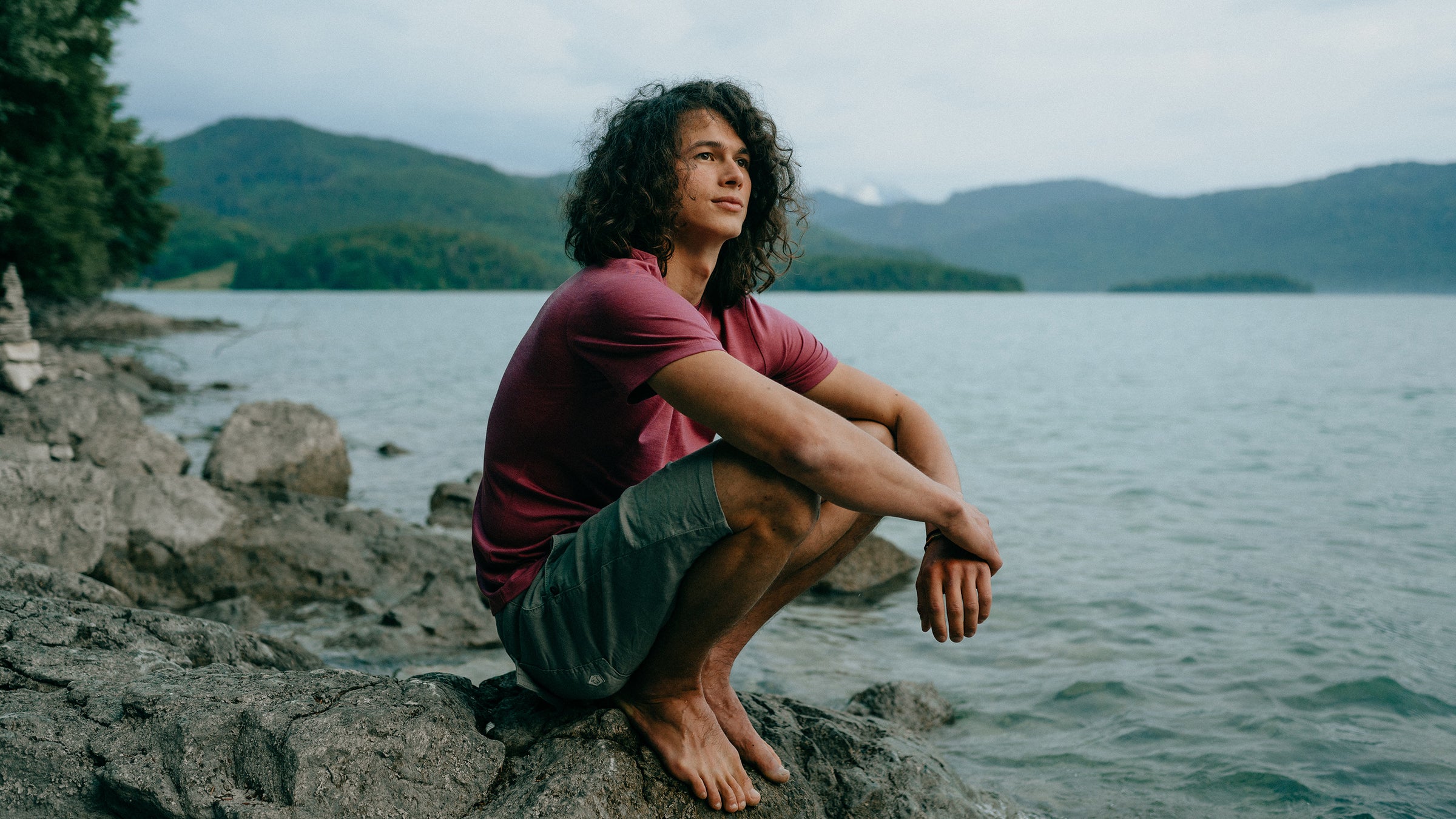 Mann mit Merino T-Shirts von Tom Fyfe sitzt am Wasser auf einem Stein