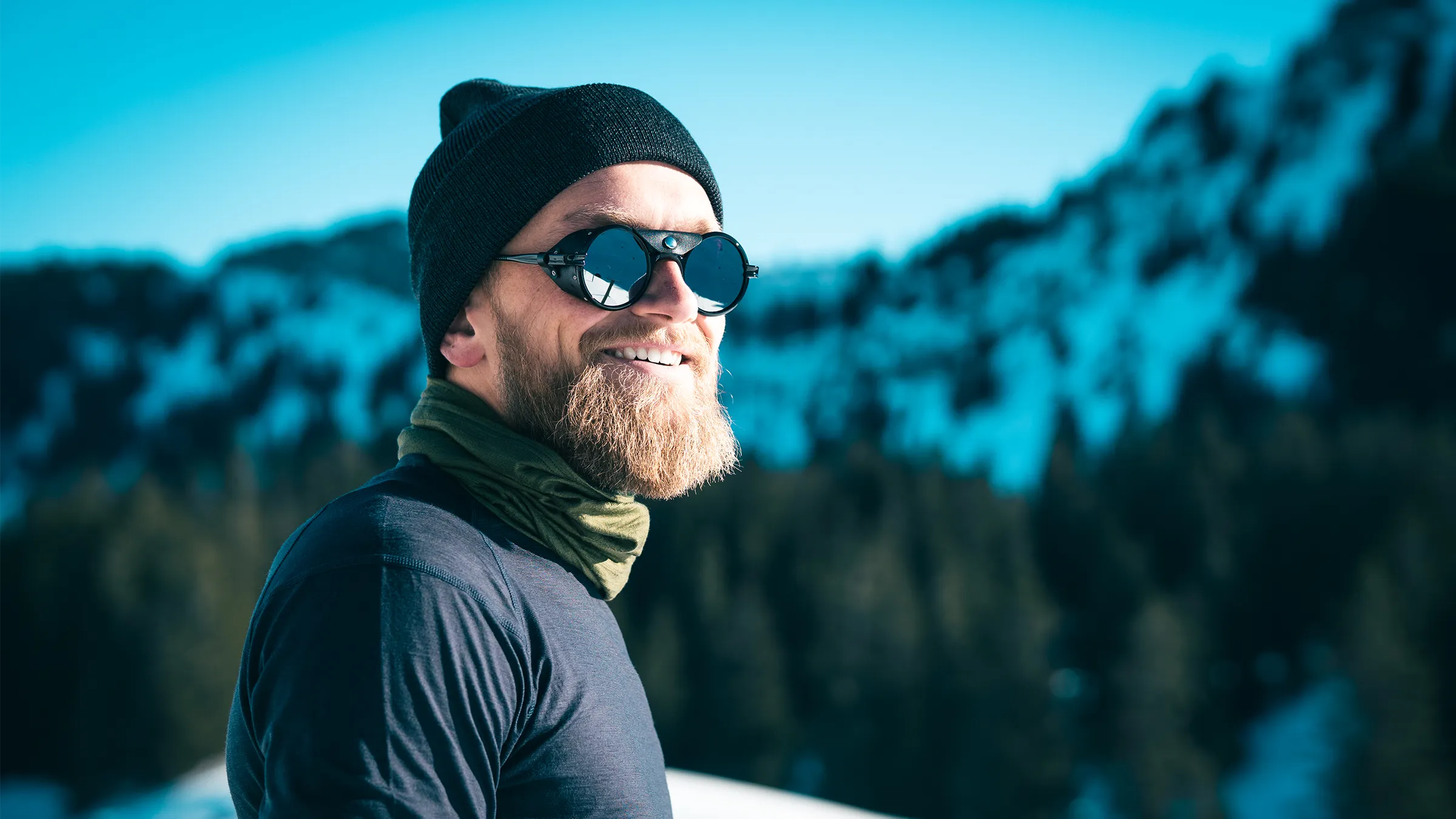 Mann mit TOM FYFE Merino Mütze und Schlauchschal vor winterlicher Berglandschaft.