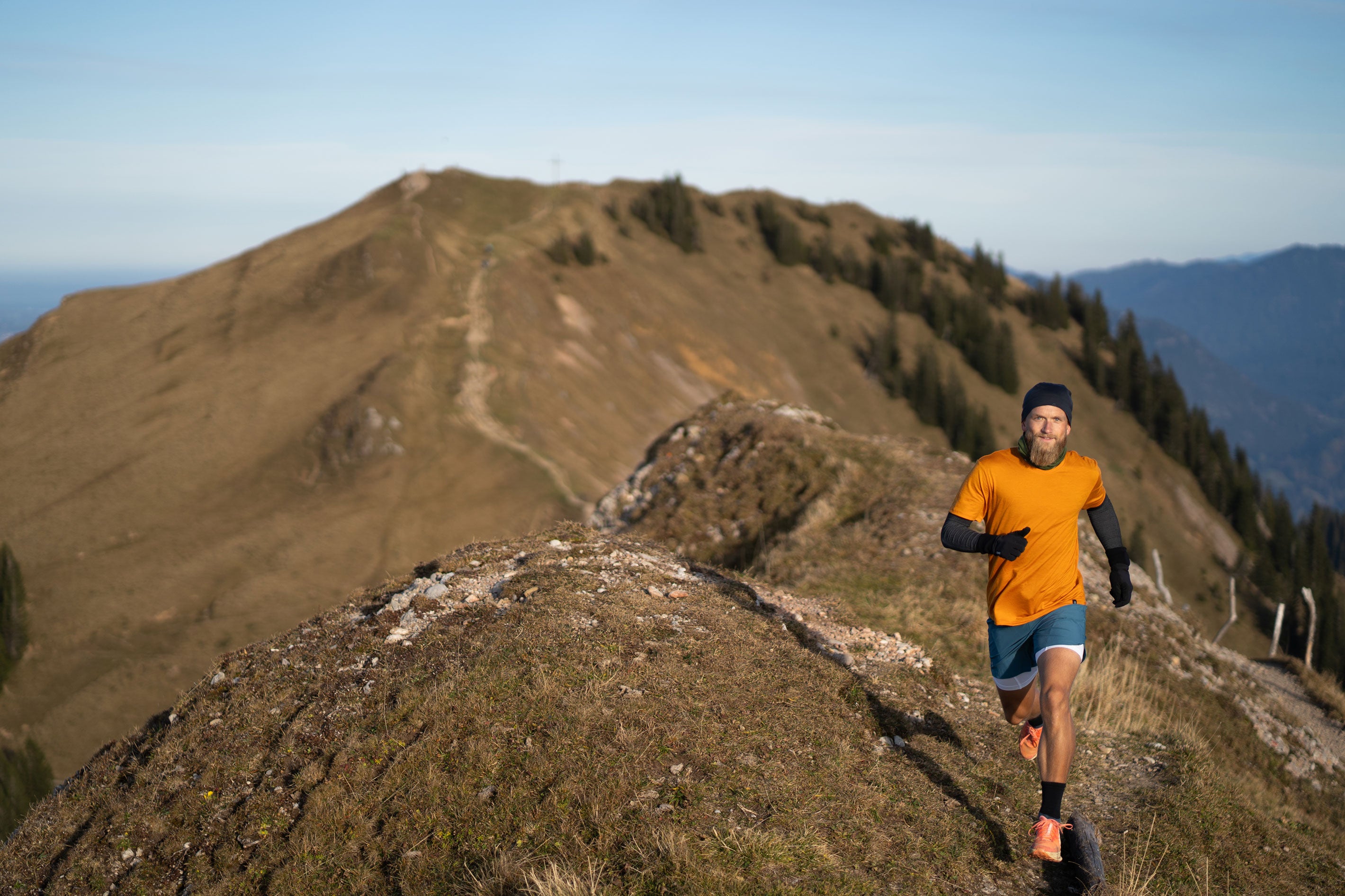 Mann in Merinokleidung von TOM FYFE läuft auf einem Berggipfel mit weiter Aussicht