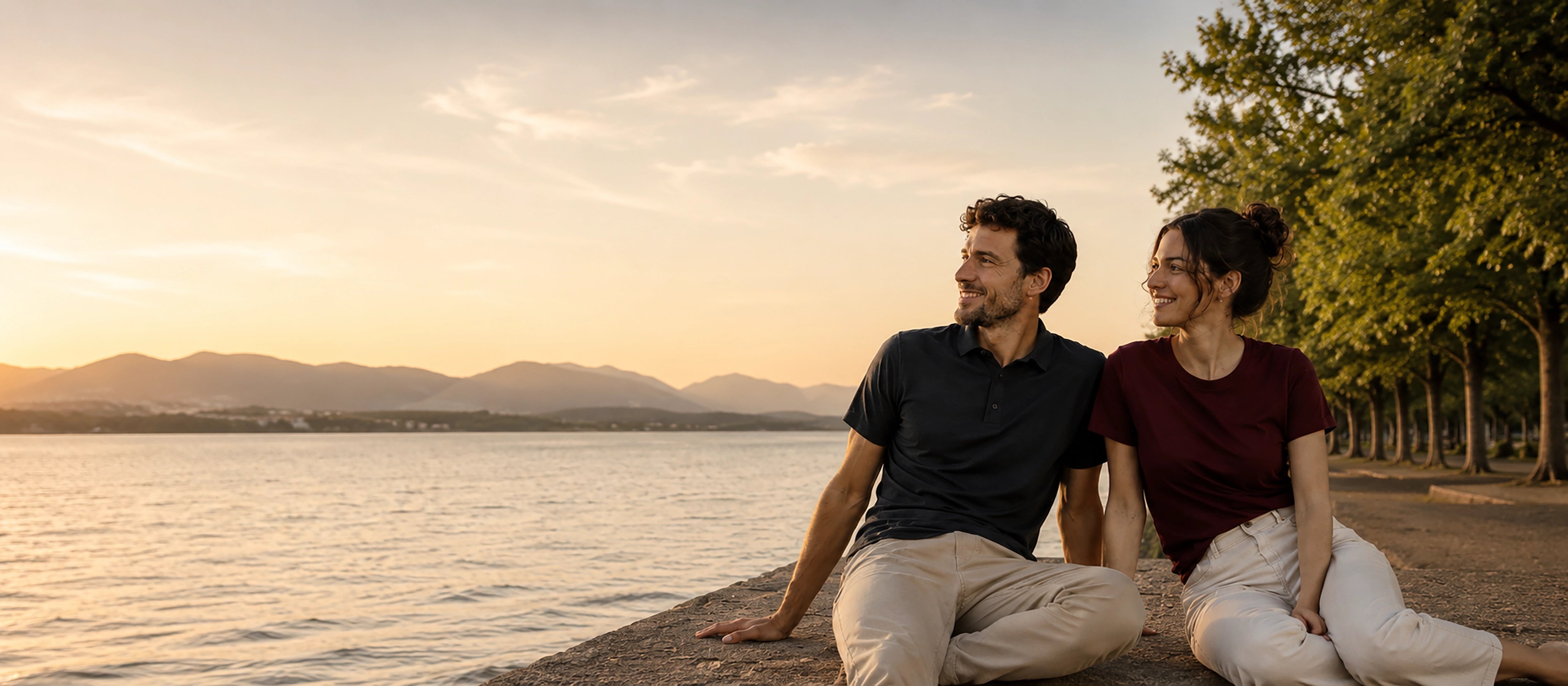 Paar in Merino-Shirt und Polo von TOM FYFE sitzt am See bei Sonnenuntergang, gekleidet für Alltag, Freizeit und entspannte Sommertage.