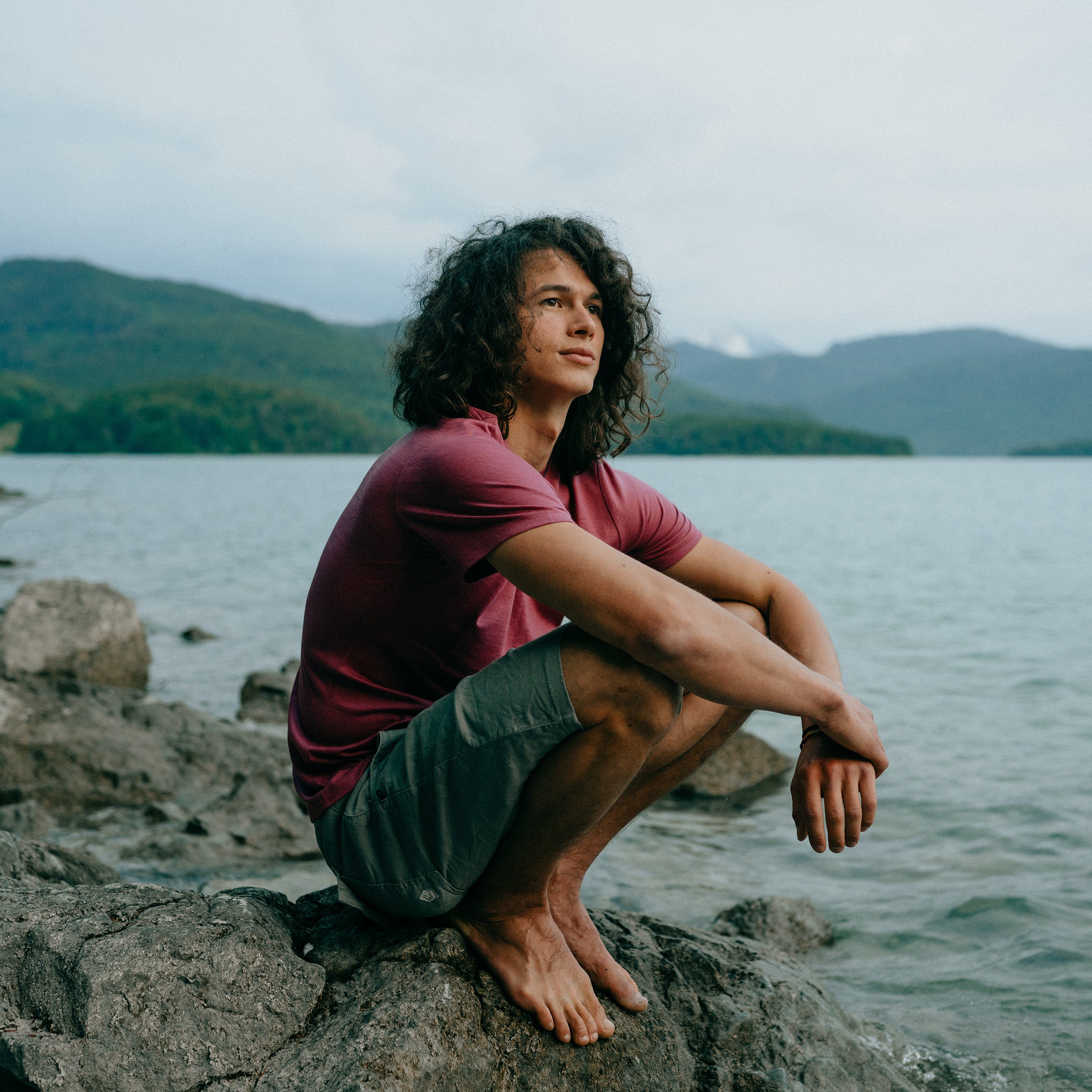 Mann mit Merino T-Shirts von Tom Fyfe sitzt am Wasser auf einem Stein