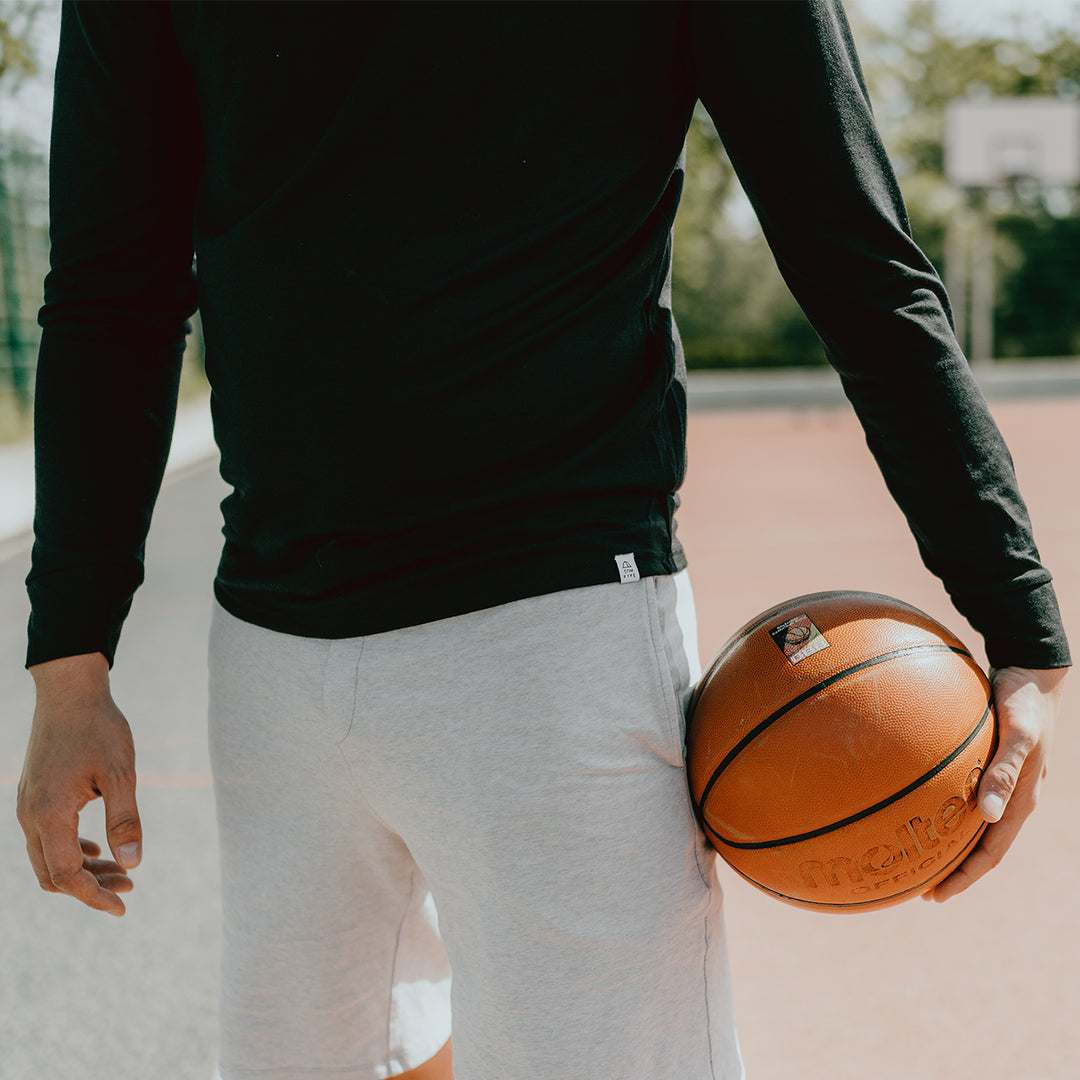 Eine Person mit langärmeligen Shirt aus Merinowolle und Basketball in der Hand