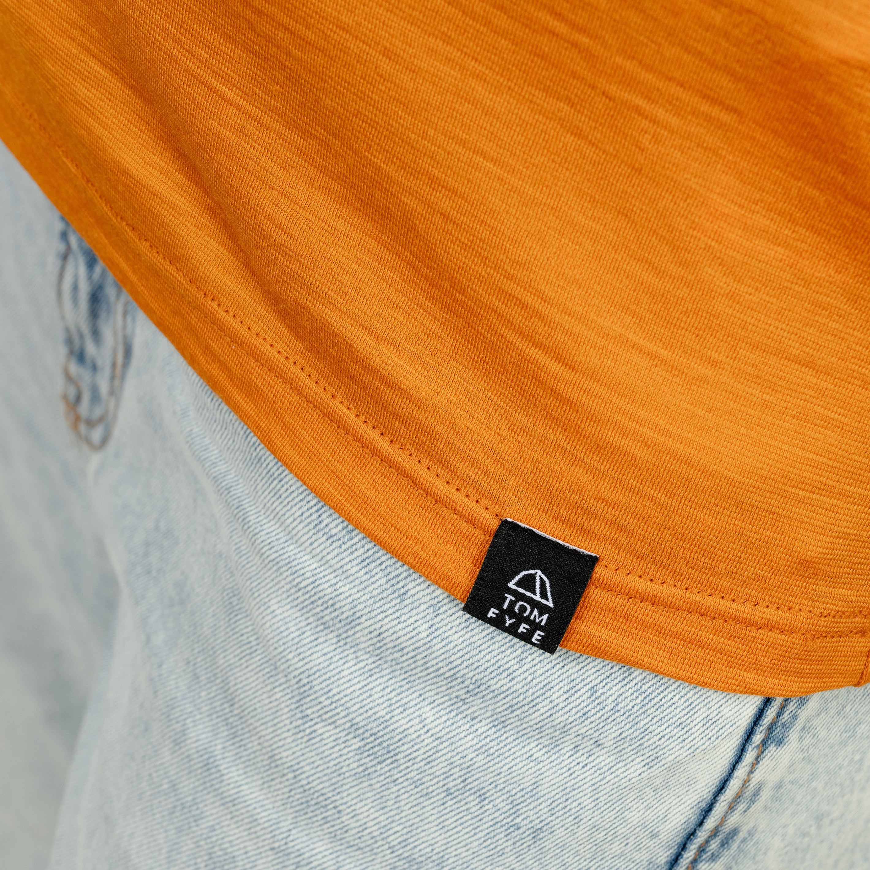 Model mit Merino Damen Shirt mit V-Ausschnitt von Tom Fyfe Saum mit angenähtem Logo in Kurkuma