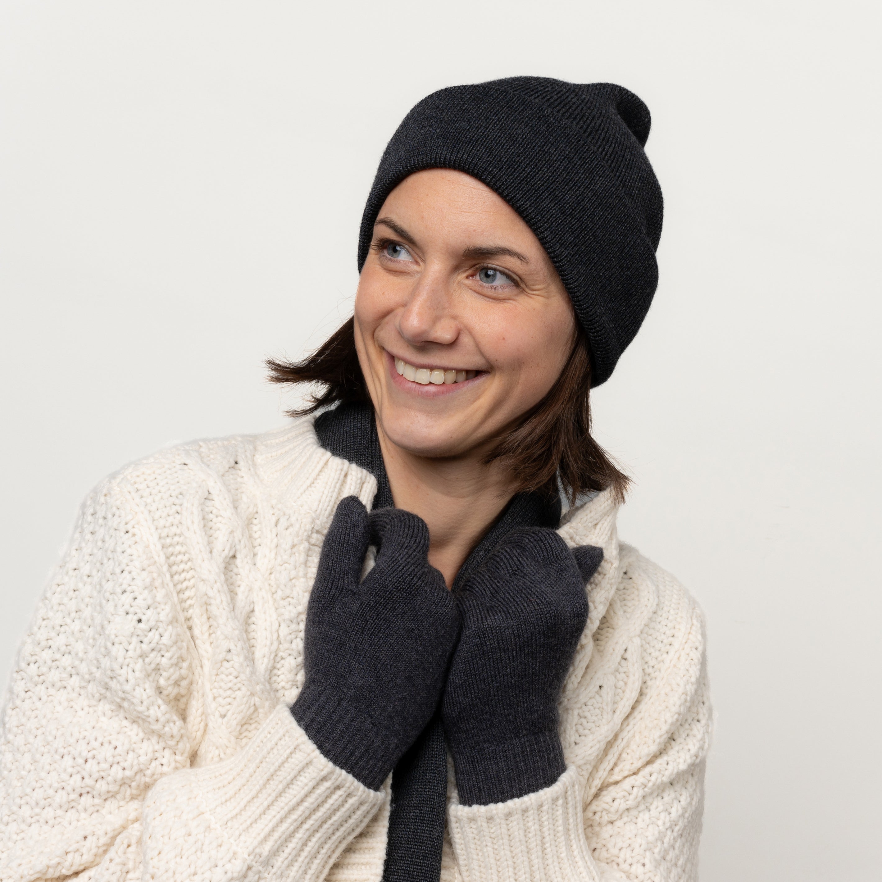 Weibliches Model fasst mit ihren Merino Strickhandschuhen von Tom Fyfe in der Farbe Anthrazit an ihren Jackenkragen