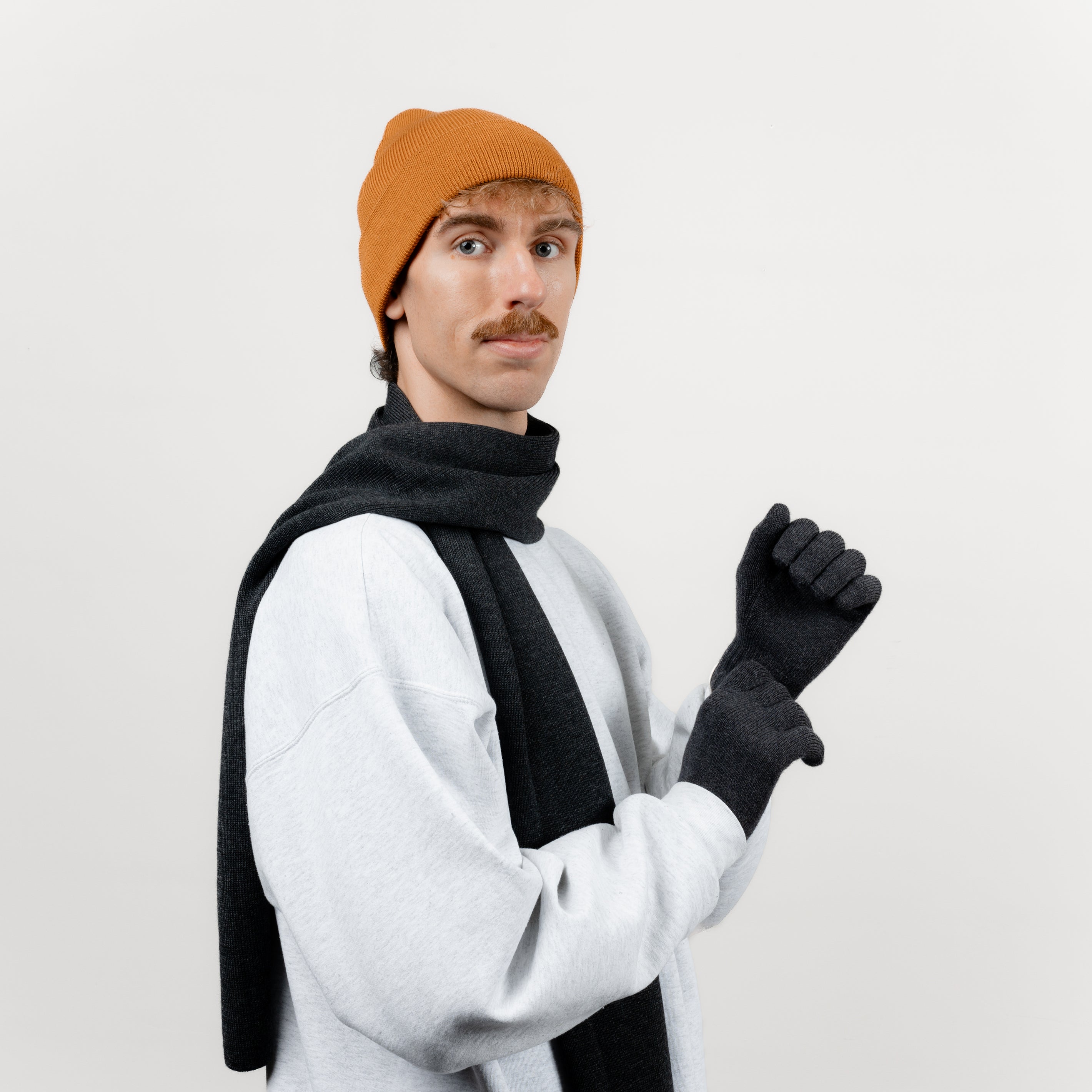 Männliches Model komibiniert Wollhandschuhe aus Merinowolle in Anthrazit mit einem passenden Schal und einer Mütze aus Wolle