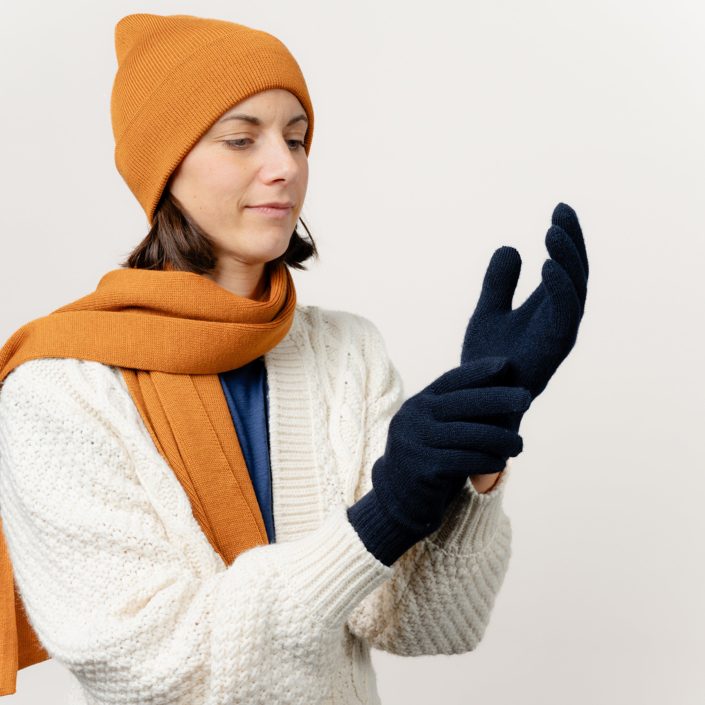 Frau zieht ihre Strickhandschuhe aus Merinowolle von Tom Fyfe in der Farbe Dunkelblau an