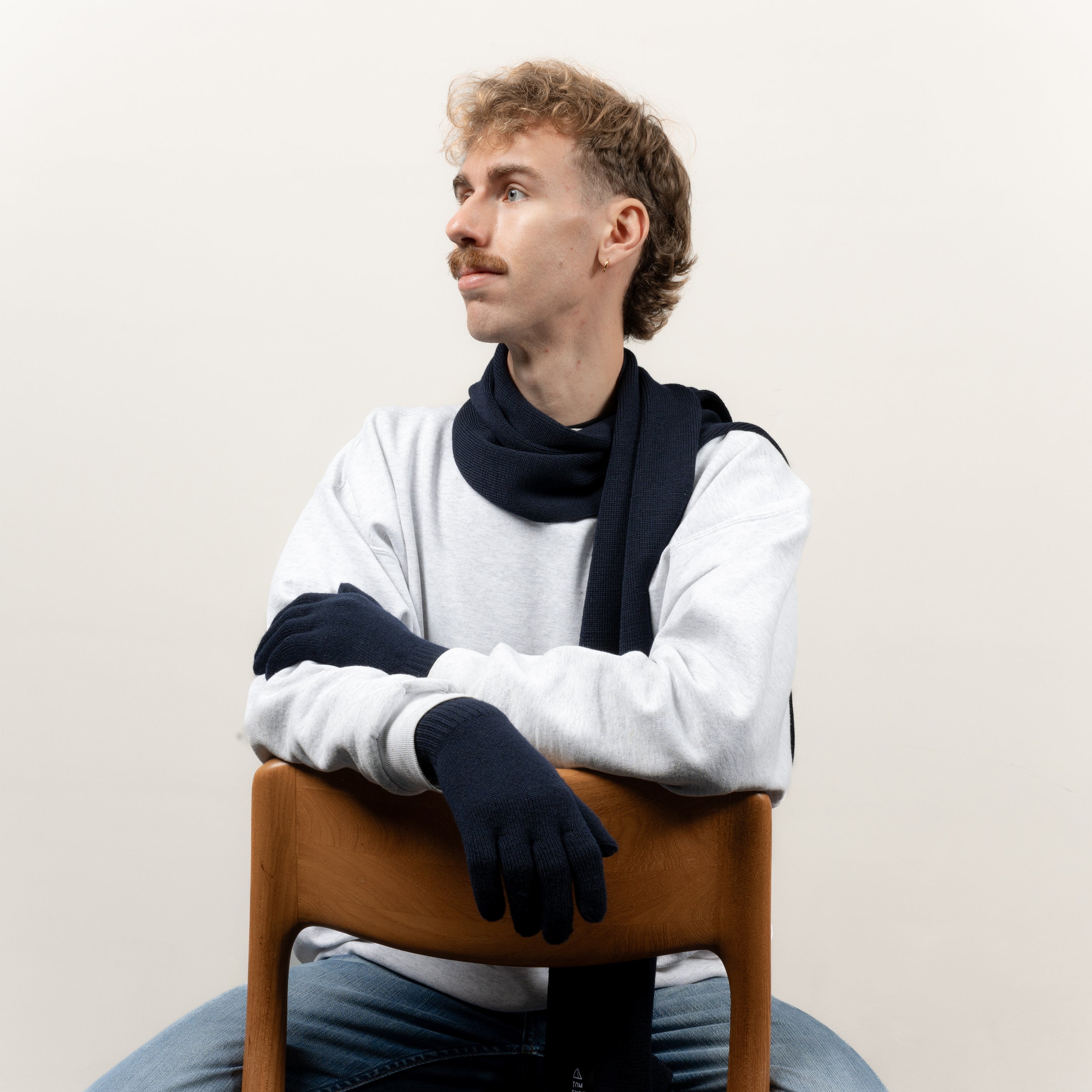 Mann mit dunkelblauen Strickhandschuhen aus Merinwolle von Tom Fyfe sitzt auf einem Stuhl