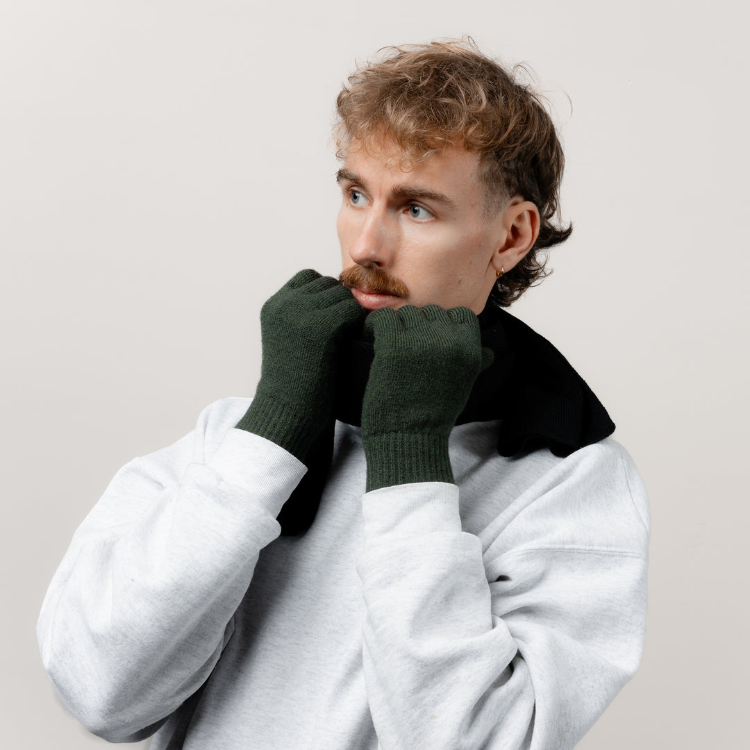 Mann fasst mit seinen Merino Strickhandschuhen von Tom Fyfe in der Farbe Dunkelgrün an seinen passenden Schal #farbe_dunkelgruen