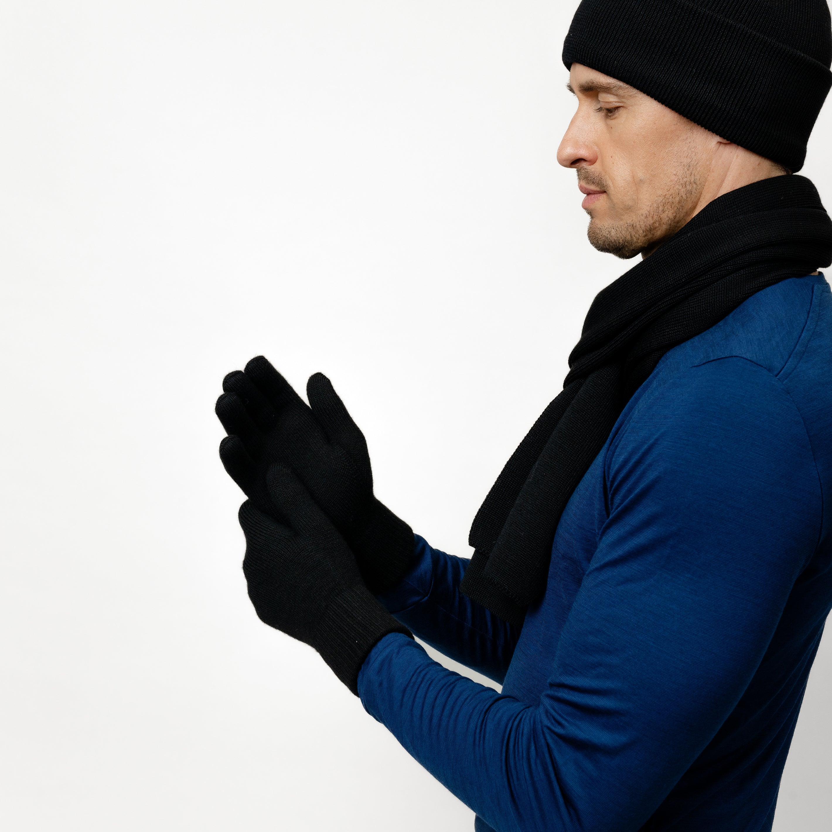 Männliches Model komibiniert Wollhandschuhe aus Merinowolle in Schwarz mit einem passenden Schal und einer Mütze aus Wolle