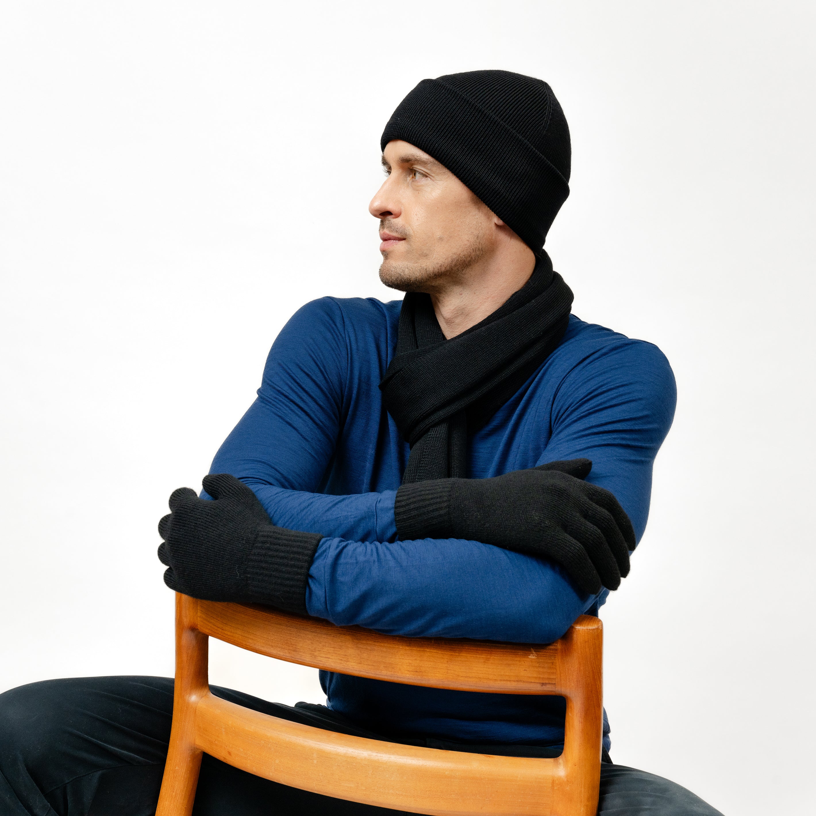 Mann mit schwarzen Strickhandschuhen aus Merinwolle von Tom Fyfe sitzt auf einem Stuhl