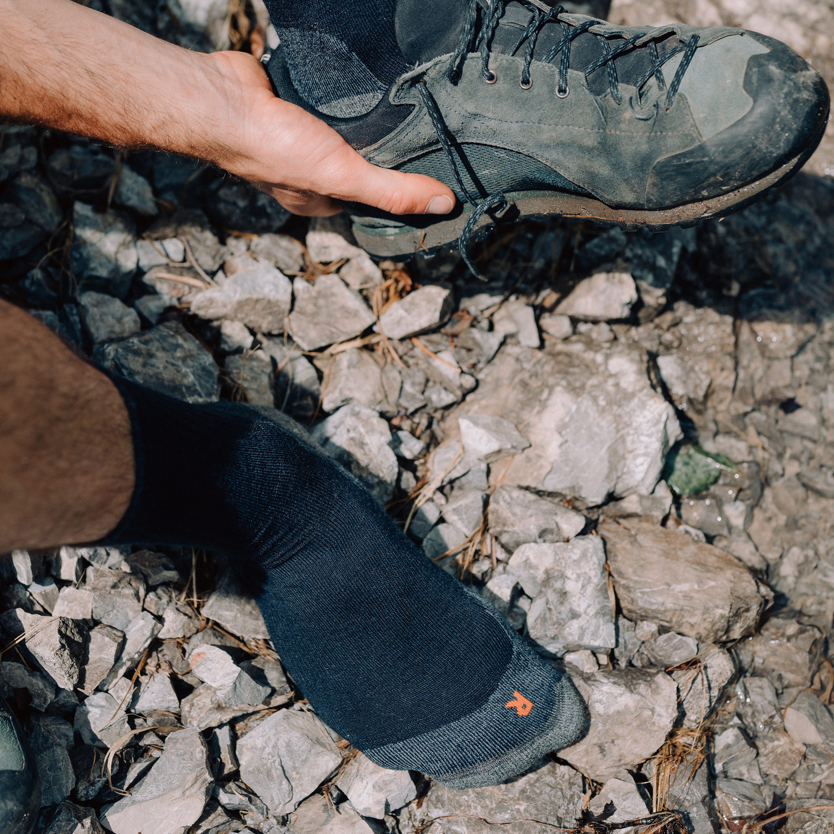 Person zieht am Flusslauf seine Wanderschuhe aus und lüftet seine Wandersocken aus Merinowolle
