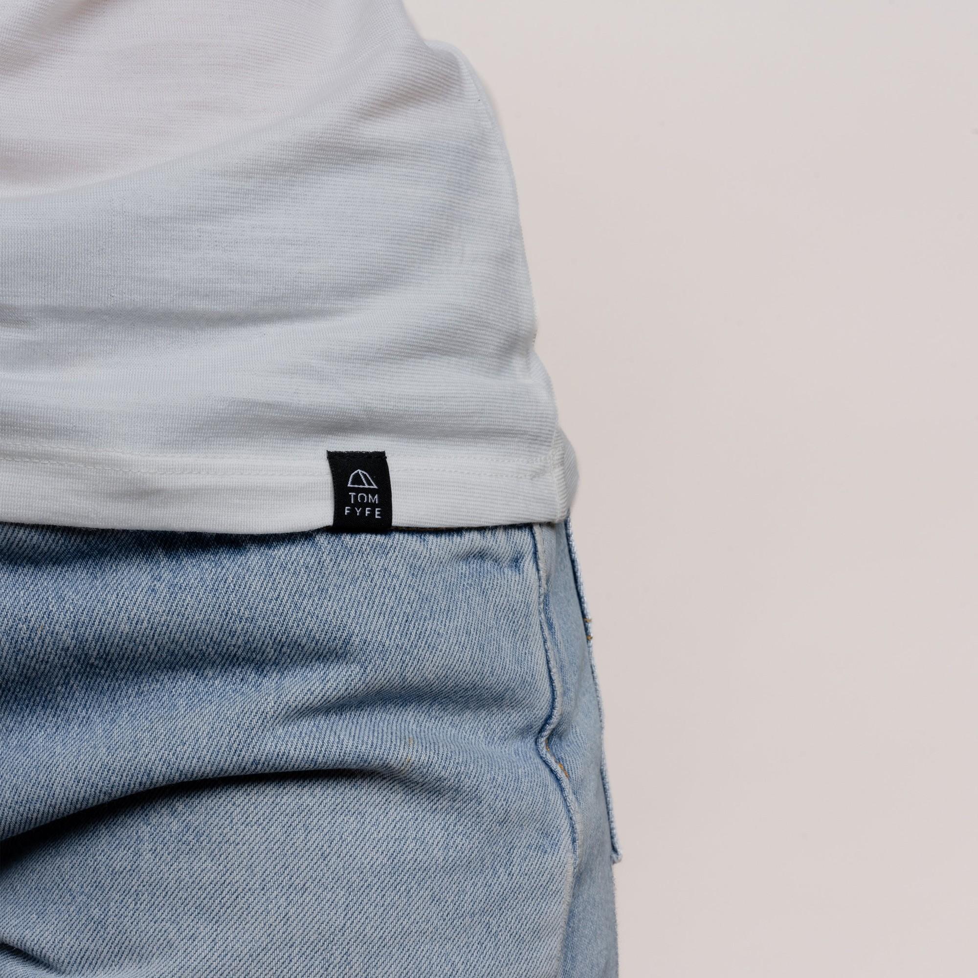 Model mit Merino Damen Shirt mit angenaehtem Stofflabel mit Logo von TOM FYFE in Weiss