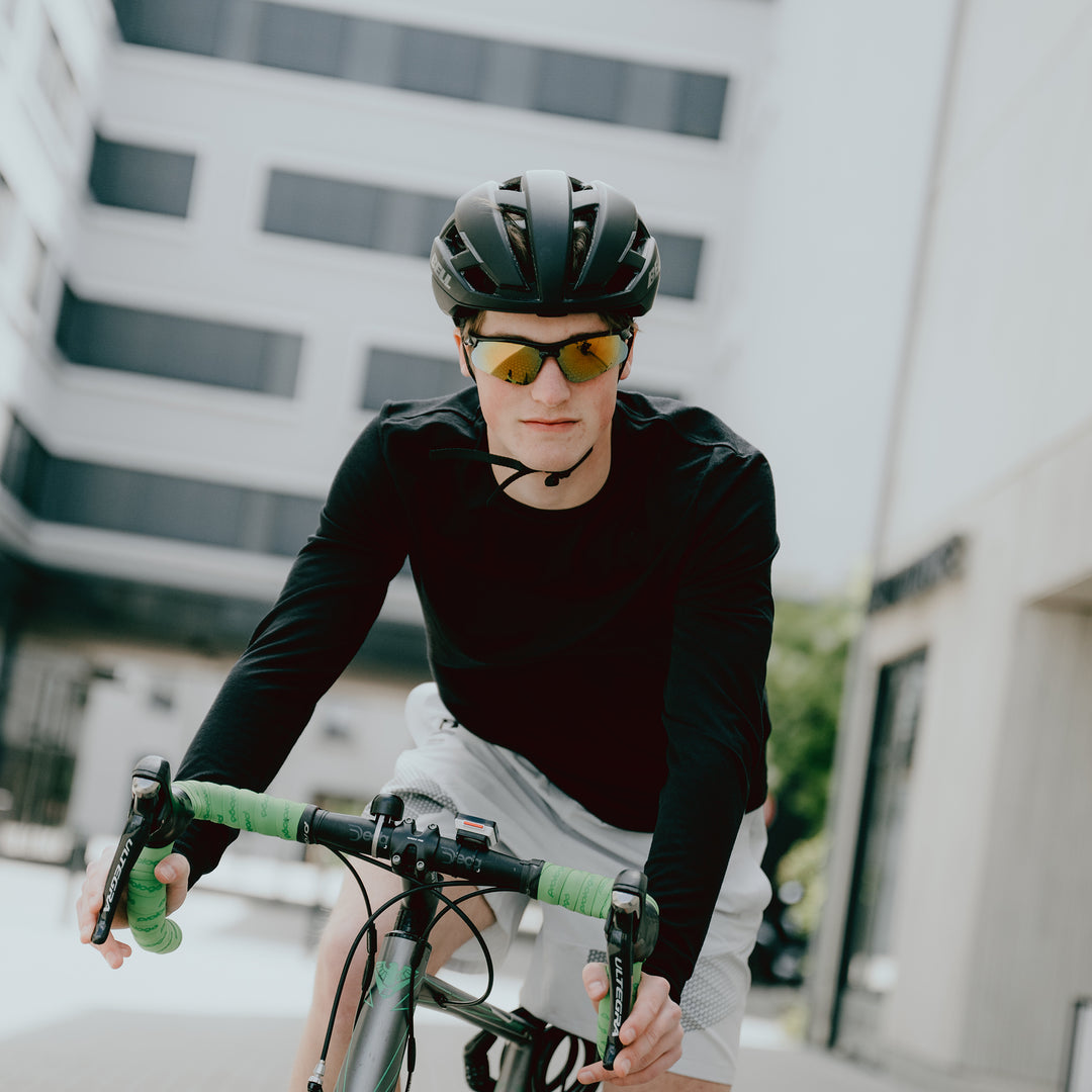 Ein Rennradfahrer fährt im Langarmshirt aus Merinowolle von Tom Fyfe durch die Stadt #farbe_schwarz