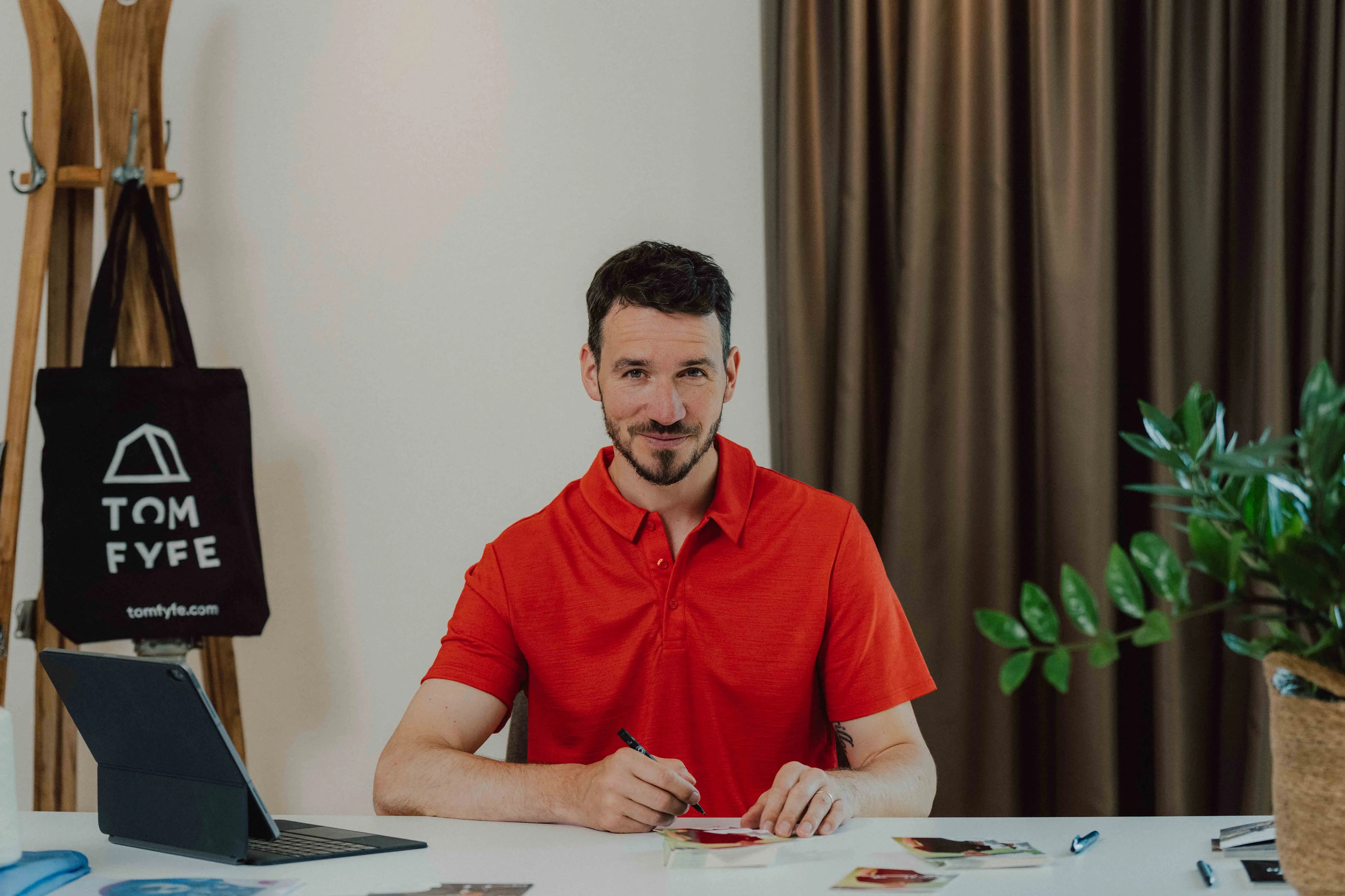 Felix Neureuther im roten TOM FYFE Merino Polo Herren am Schreibtisch.