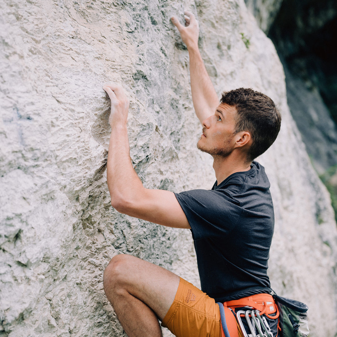 Mann klettert am Fels und trägt ein T-shirt aus Merinowolle von Tom Fyfe #farbe_anthrazit