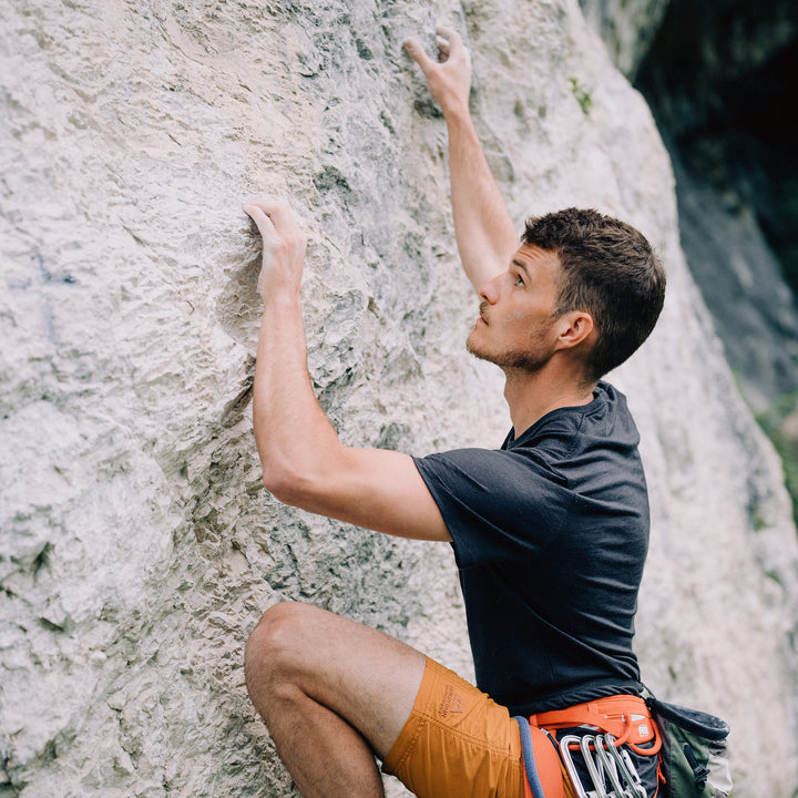 Mann klettert am Fels und trägt ein T-shirt aus Merinowolle von Tom Fyfe #farbe_brombeere
