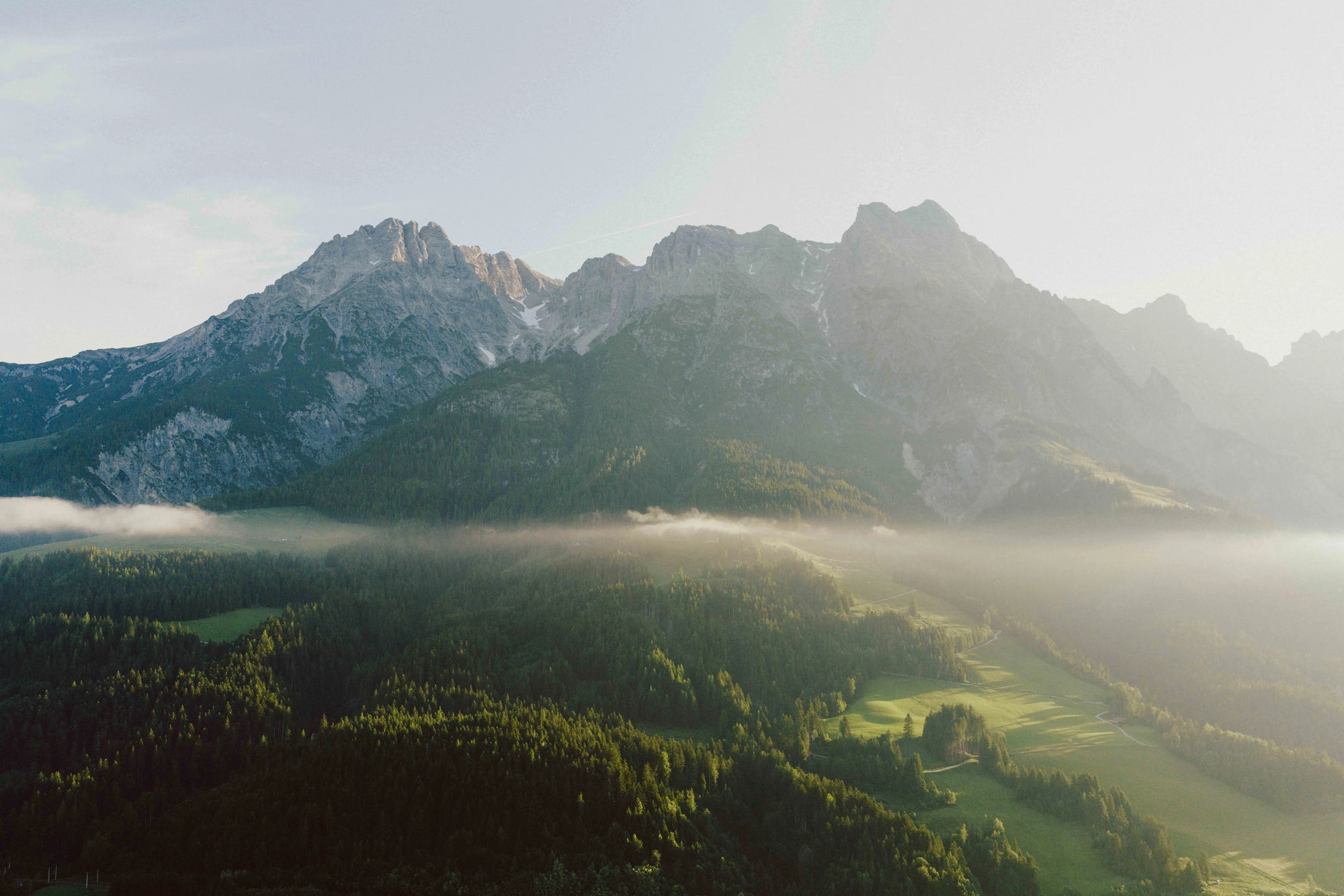 Alpenlandschaft mit Bergen, Wald und Nebel im Sonnenaufgang als TOM FYFE Outdoor-Motiv.