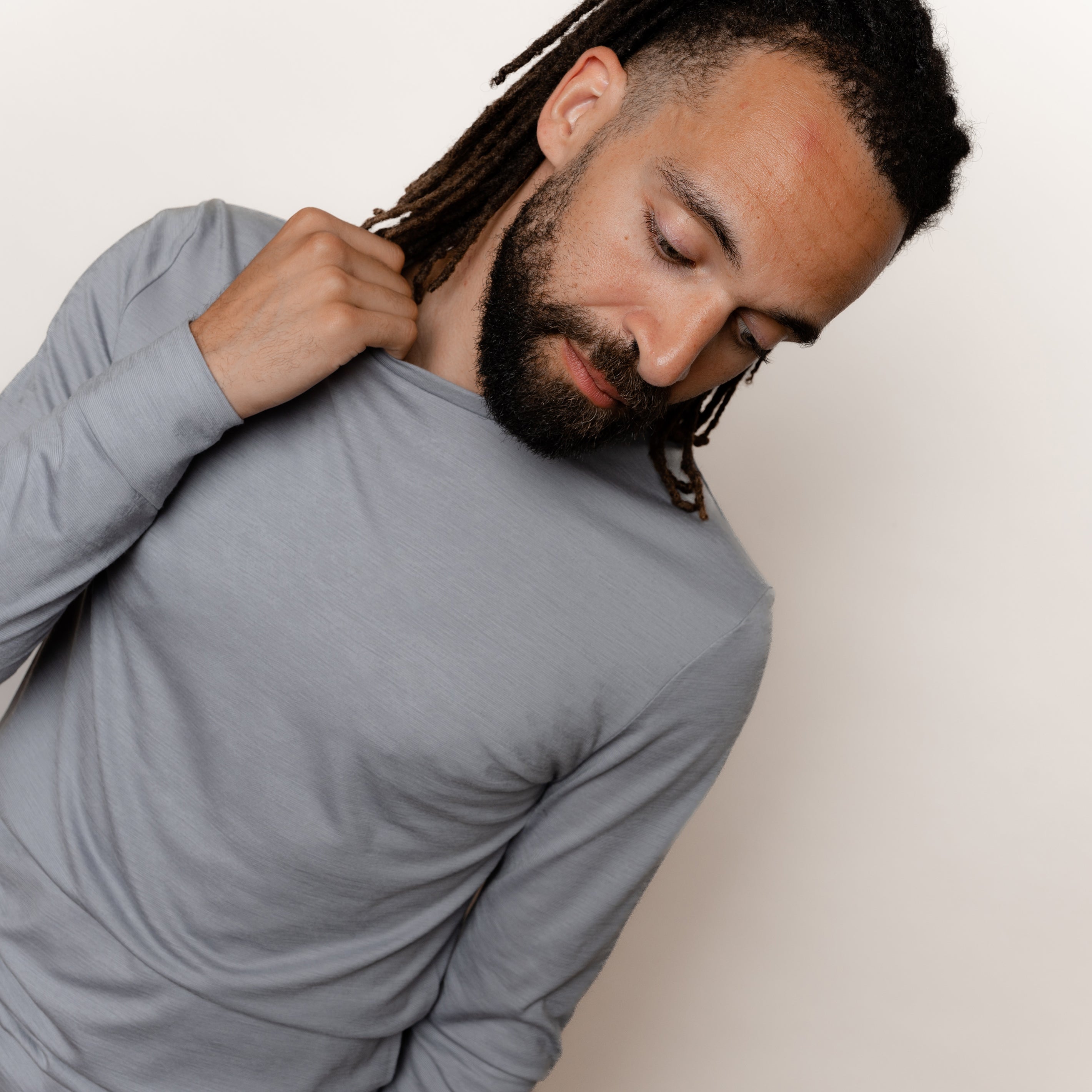 Maennliches Model greift in den Kragen seines Merino Herren Longsleeve von Tom Fyfe in Hellgrau #farbe_hellgrau