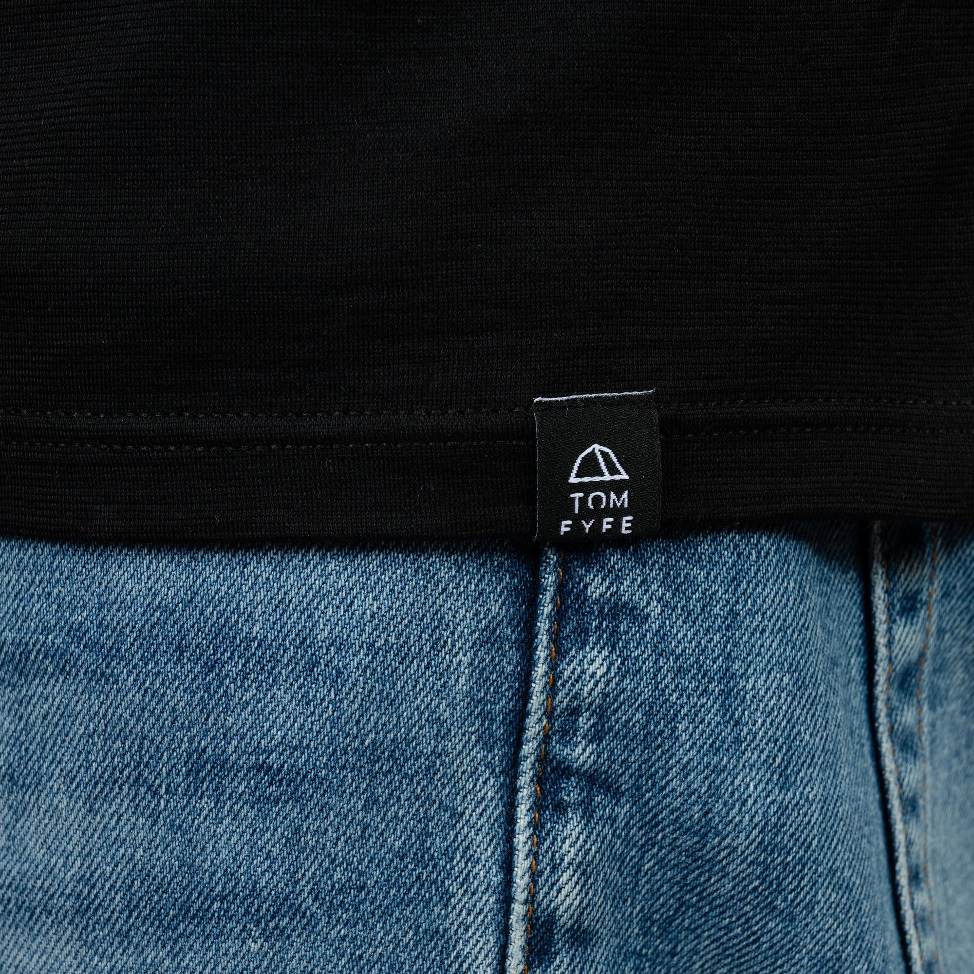 Model mit Merino Herren Poloshirt Label von Tom Fyfe in Schwarz 