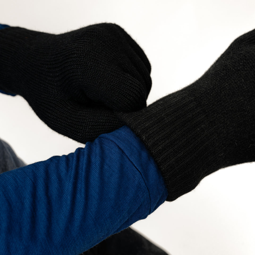 Männliches Model zieht seine Strickhandschuhe aus Merinowolle von Tom Fyfe in der Farbe Schwarz an. Dazu trägt es ein Longsleeve aus Merinowolle von Tom Fyfe #farbe_schwarz