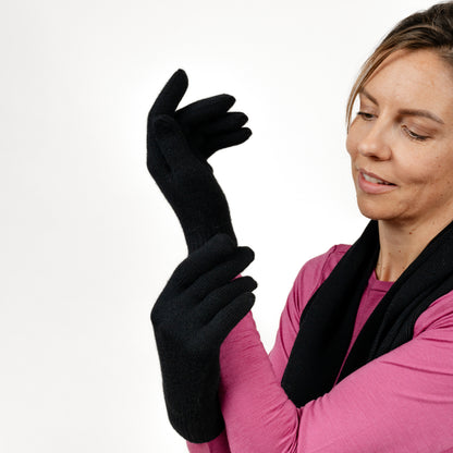 Weibliches Model fasst mit ihren Merino Strickhandschuhen von Tom Fyfe in der Farbe Schwarz an ihren Arm 