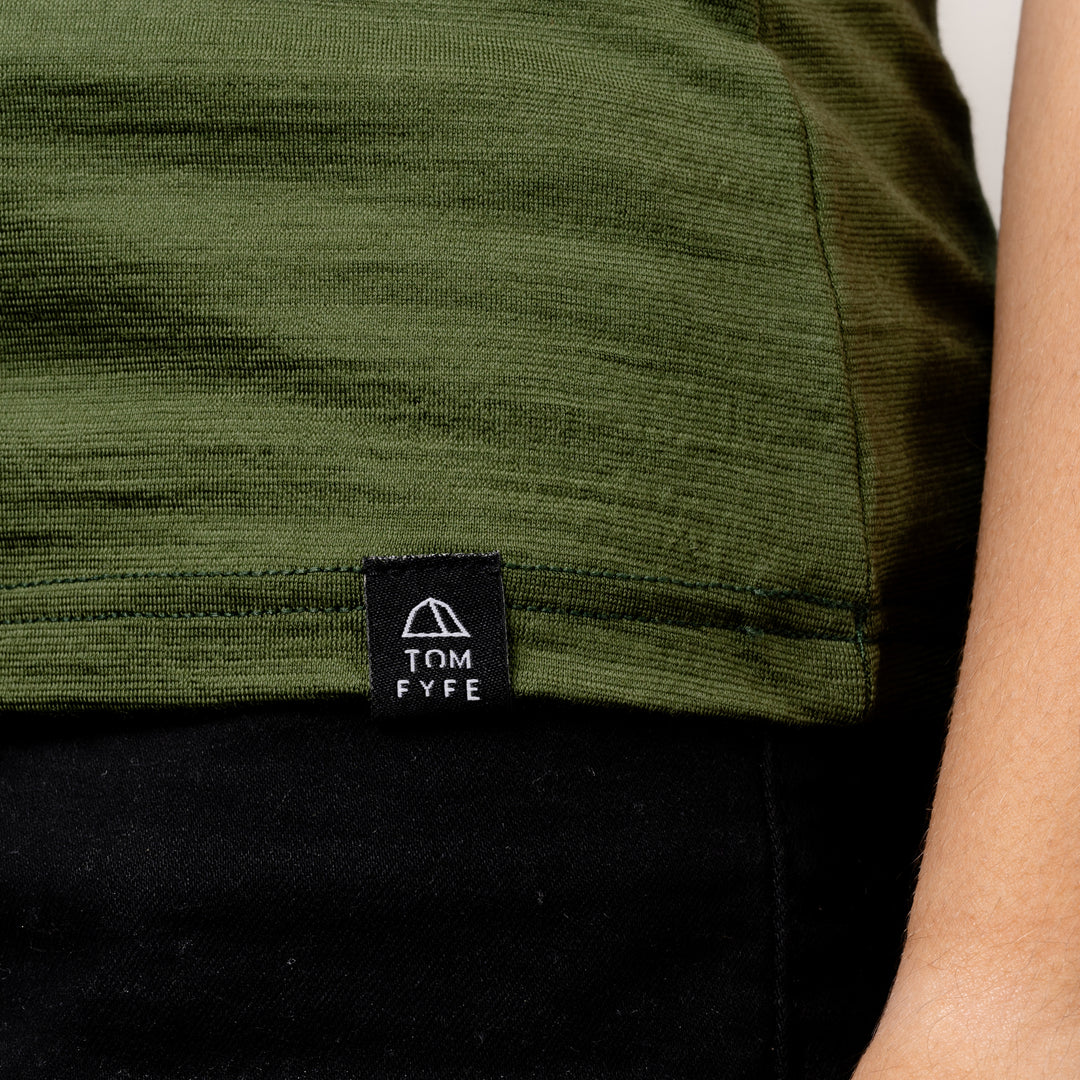 Model im Merino Damen Shirt mit Ausschnitt von Tom Fyfe in Wadgrün Saum mit angenähtem Logo #farbe_waldgruen