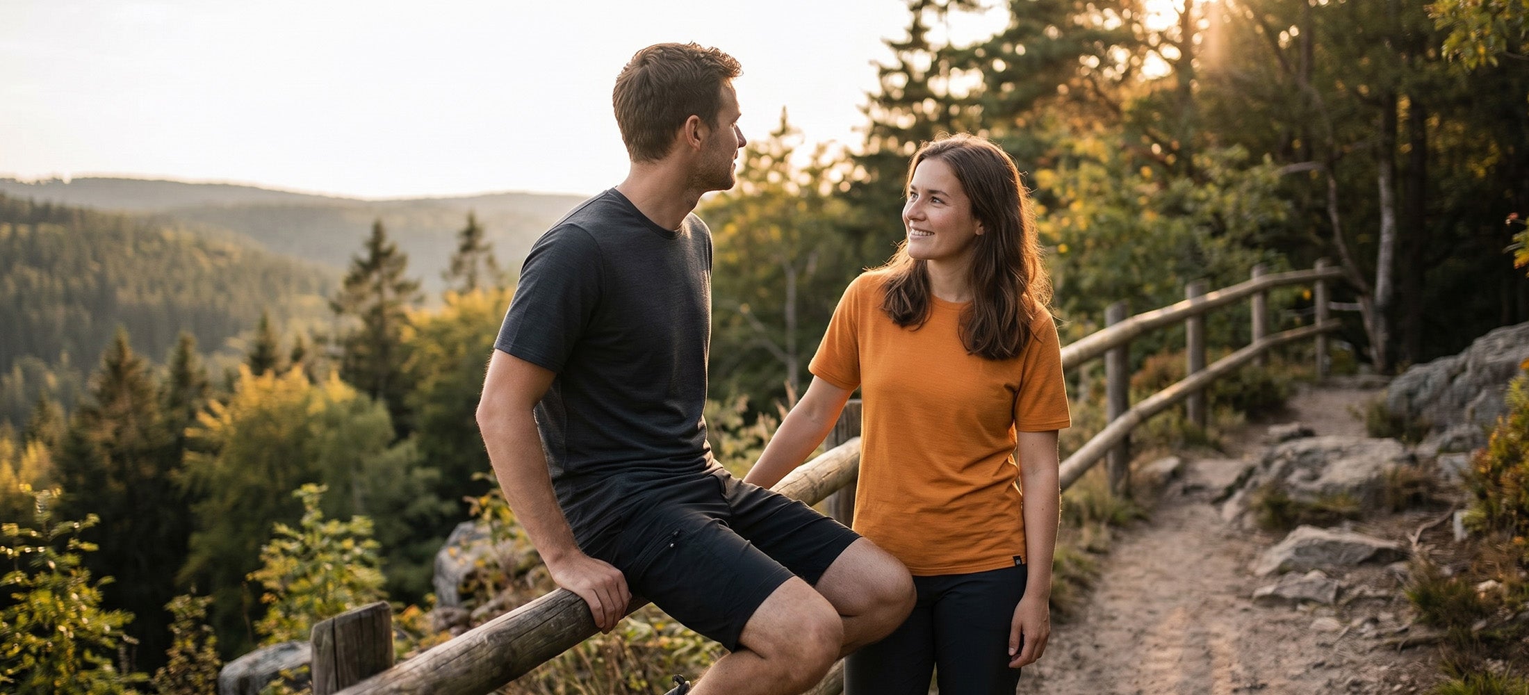 Paar in Merino-Shirts an einem Wanderweg in sonniger Waldlandschaft
